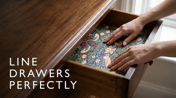 Hands fitting a decorative William Morris liner into an antique drawer, illustrating how to line drawers.